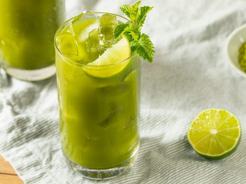 Matcha Lime Lemonade in einem Glas mit Eiswürfeln, daneben ein Limettenschnitz.