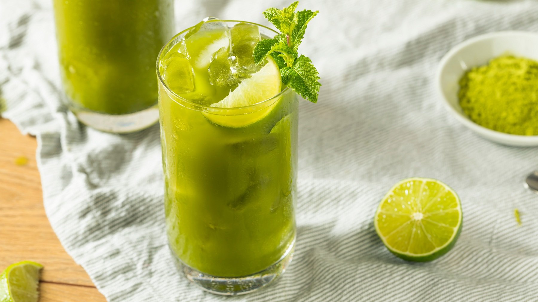 Matcha Lime Lemonade in einem Glas mit Eiswürfeln, daneben ein Limettenschnitz.