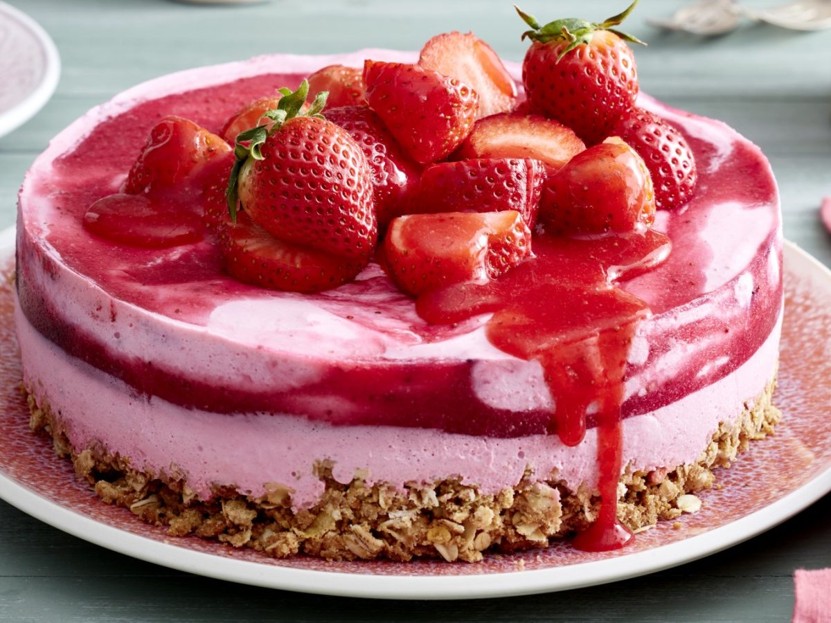 Müsli-Erdbeertorte mit frischen Erdbeeren und Sauce darauf auf einem rosa Teller.