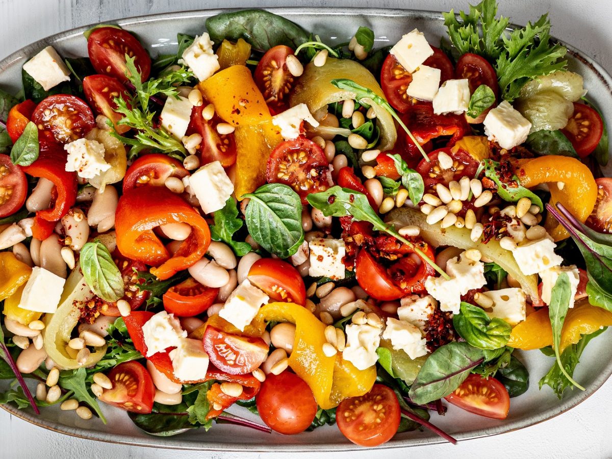 Paprikasalat mit Bohnen, Pinienkernen, Tomaten und Feta von oben fotografiert.