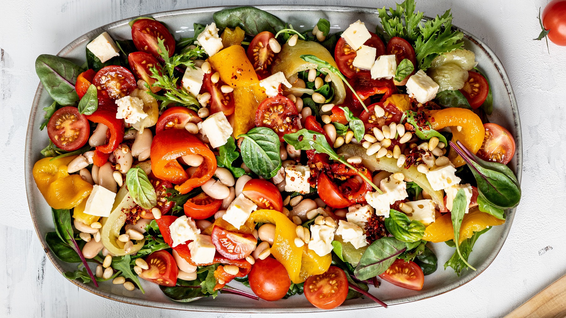 Paprikasalat mit Bohnen, Pinienkernen, Tomaten und Feta von oben fotografiert.