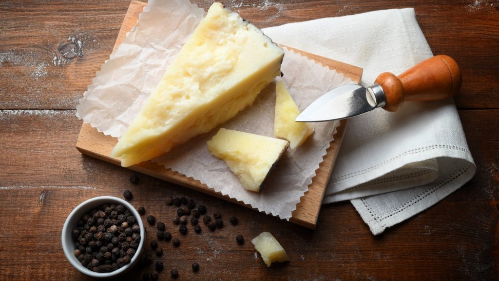 Pecorino siciliano auf einem Brett mit Käsemesser und Schale mit Pfefferkörnern.