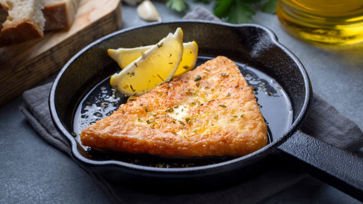 Saganaki in einer gusseisernen Pfanne mit einer Zitronenspalte.