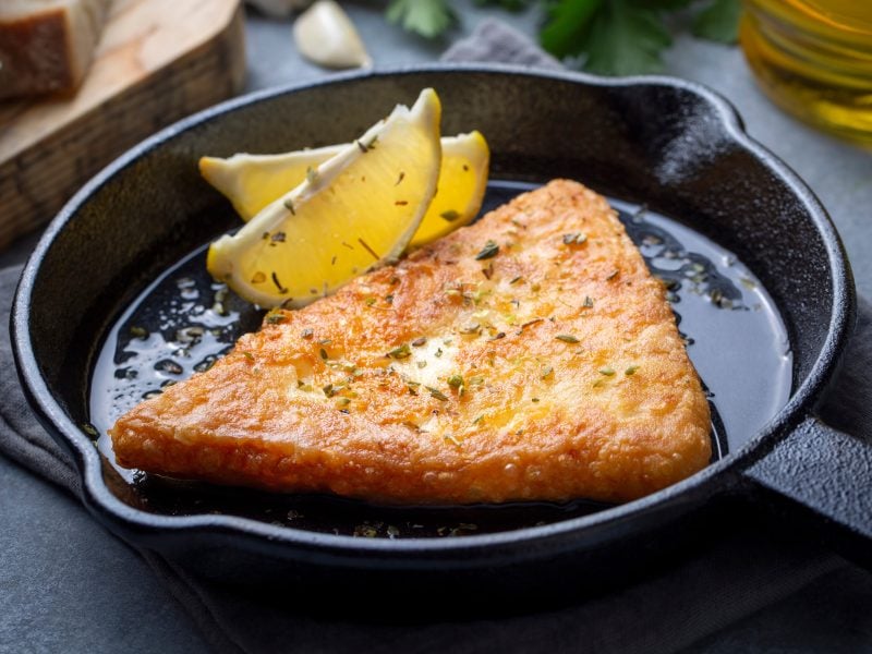 Saganaki in einer gusseisernen Pfanne mit einer Zitronenspalte.