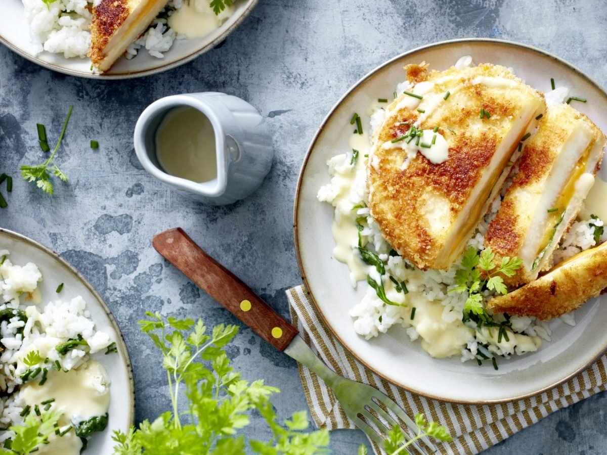 Teilweise Ansicht von drei Tellern mit Sellerie-Cordon-bleu, Reis, heller Sauce und Kräutern.