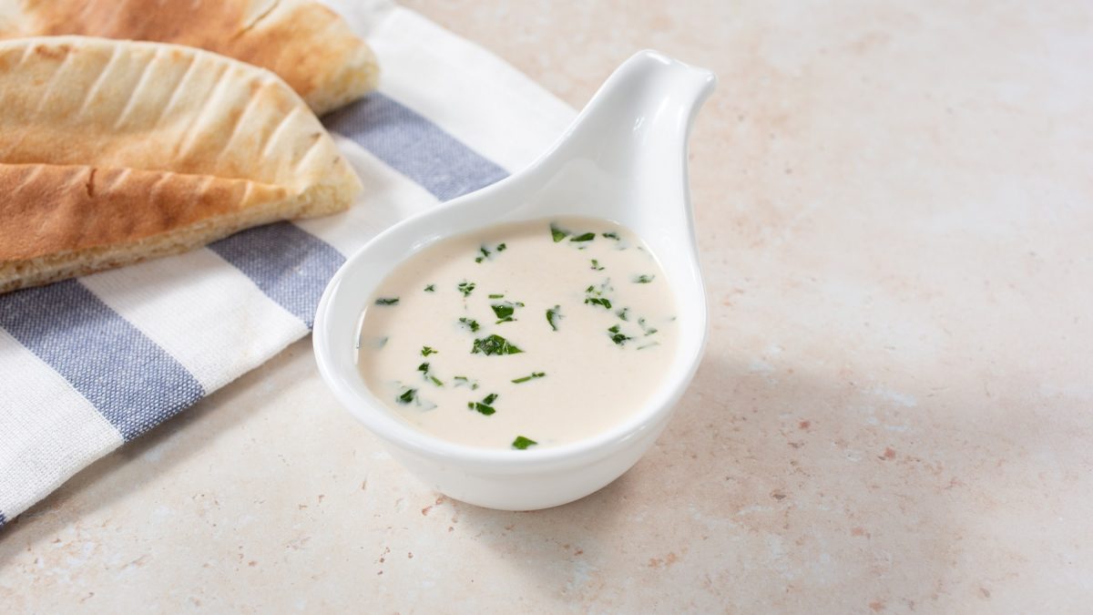 Tahini-Dressing in einer weißen Servierschale, im Hintergrund Fladenbrot.