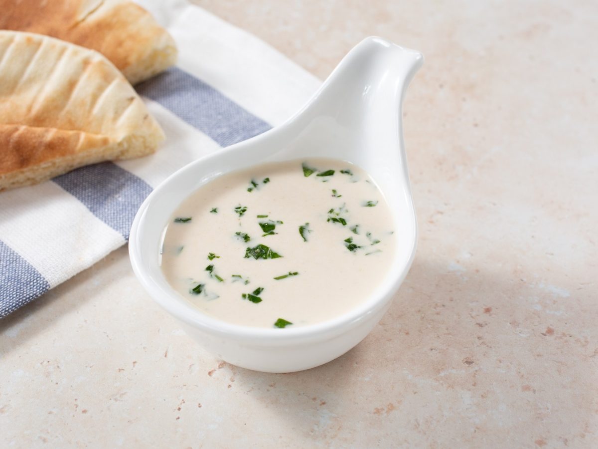 Tahini-Dressing in einer weißen Servierschale, im Hintergrund Fladenbrot.