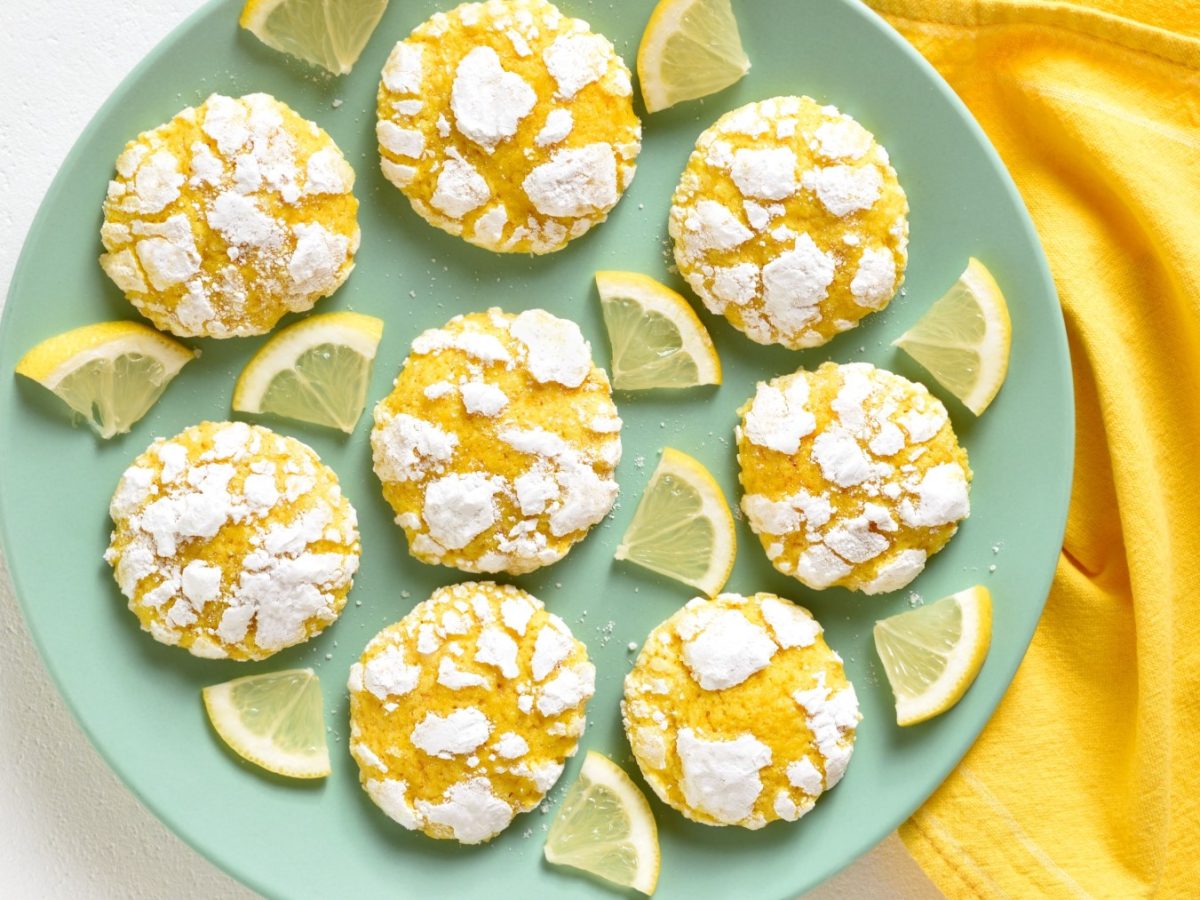 Zitronen-Cookies ohne Mehl auf einem türkisfarbenen Teller auf einem weißen Hintergrund. Rechts auf dem Bild ein gelbes Geschirrtuch.