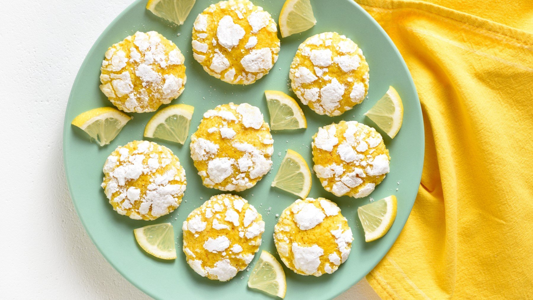 Zitronen-Cookies ohne Mehl auf einem türkisfarbenen Teller auf einem weißen Hintergrund. Rechts auf dem Bild ein gelbes Geschirrtuch.