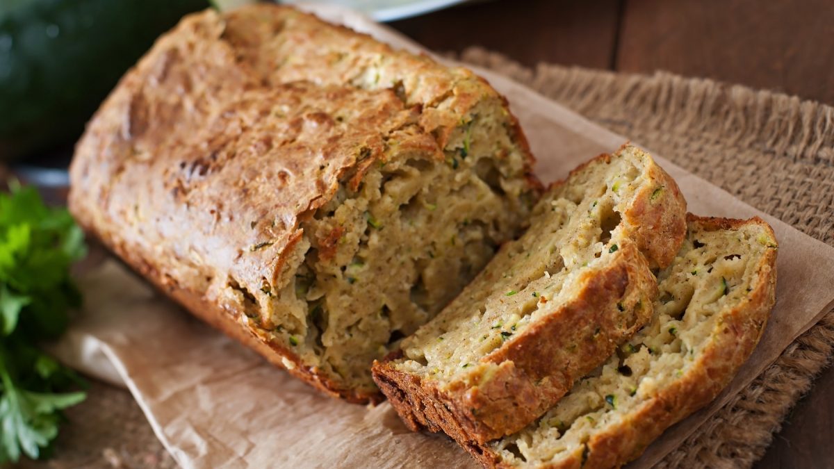 Das angeschnittene Brot auf etwas Backpapier und rustikalem Holzuntergrund. Alles von schräg oben fotografiert.