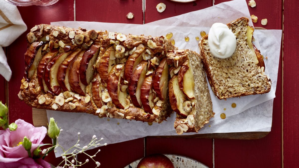 Apfel-Hafer-Kuchen auf weißem Backpapier auf rotem Hintergrund. Links unten auf dem Foto Blumen.