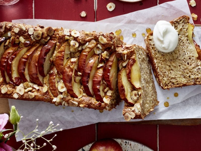 Apfel-Hafer-Kuchen auf weißem Backpapier auf rotem Hintergrund. Links unten auf dem Foto Blumen.