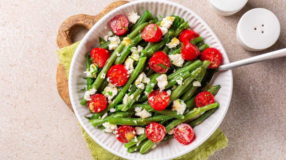 Draufsicht: Ein Bohnensalat mit Feta auf einem weißen Teller. der steht auf einem hellen Untergrund. Daneben steht ein Salzstreuer.