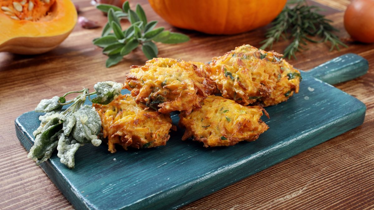 Frittelle di zucca auf einem blauen Brettchen, daneben frittierter Salbei.