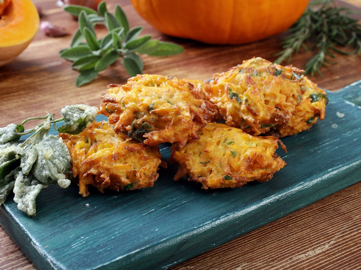 Frittelle di zucca auf einem blauen Brettchen, daneben frittierter Salbei.