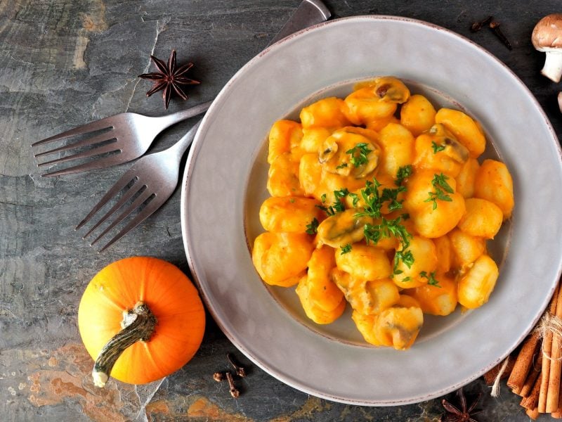 Gnocchi mit Kürbissauce und Champignons auf einem weißen Teller, daneben ein Kürbis und Gewürze, von oben fotografiert.