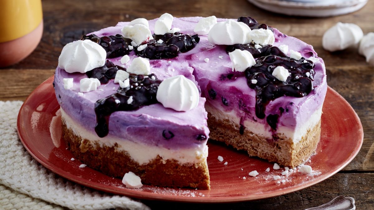 Angeschnittene Heidelbeer-Skyr-Torte mit Baiser auf rotem Teller.