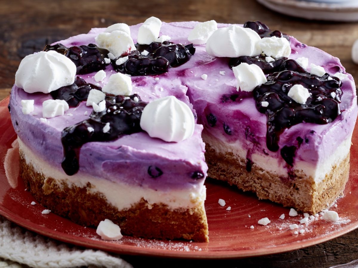 Angeschnittene Heidelbeer-Skyr-Torte mit Baiser auf rotem Teller.