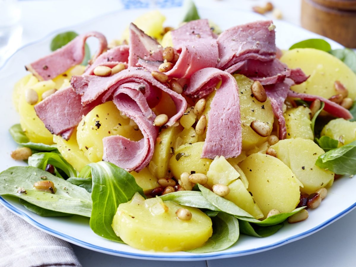 Kartoffelsalat mit Roastbeef auf einem weißen Teller auf hellem Hintergrund.