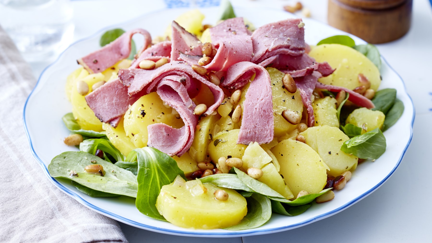 Kartoffelsalat mit Roastbeef auf einem weißen Teller auf hellem Hintergrund.