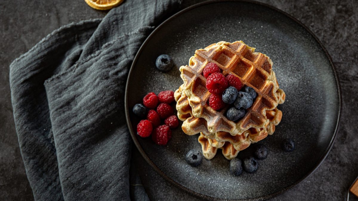 Lütticher Waffeln mit frischen Beeren und Puderzucker auf einem schwarzen Teller von oben fotografiert.