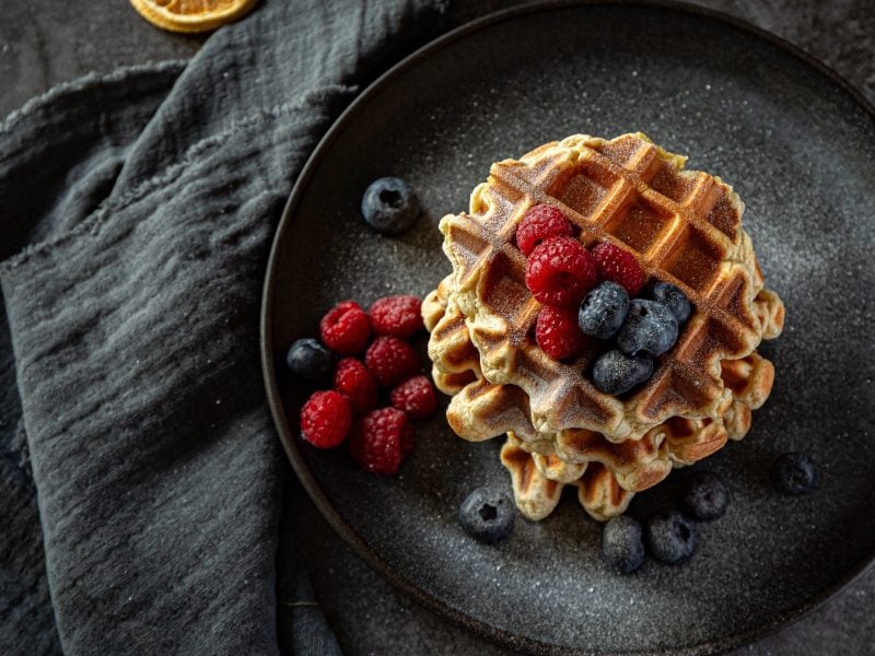 Lütticher Waffeln mit frischen Beeren und Puderzucker auf einem schwarzen Teller von oben fotografiert.