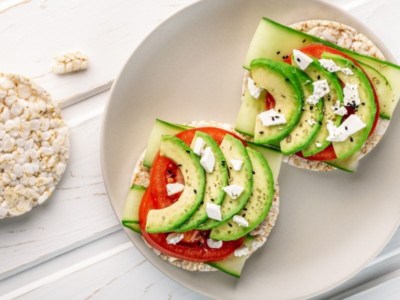 Reiswaffeln mit Avocado und Feta auf einem beigen Teller auf weißem Hintergrund.