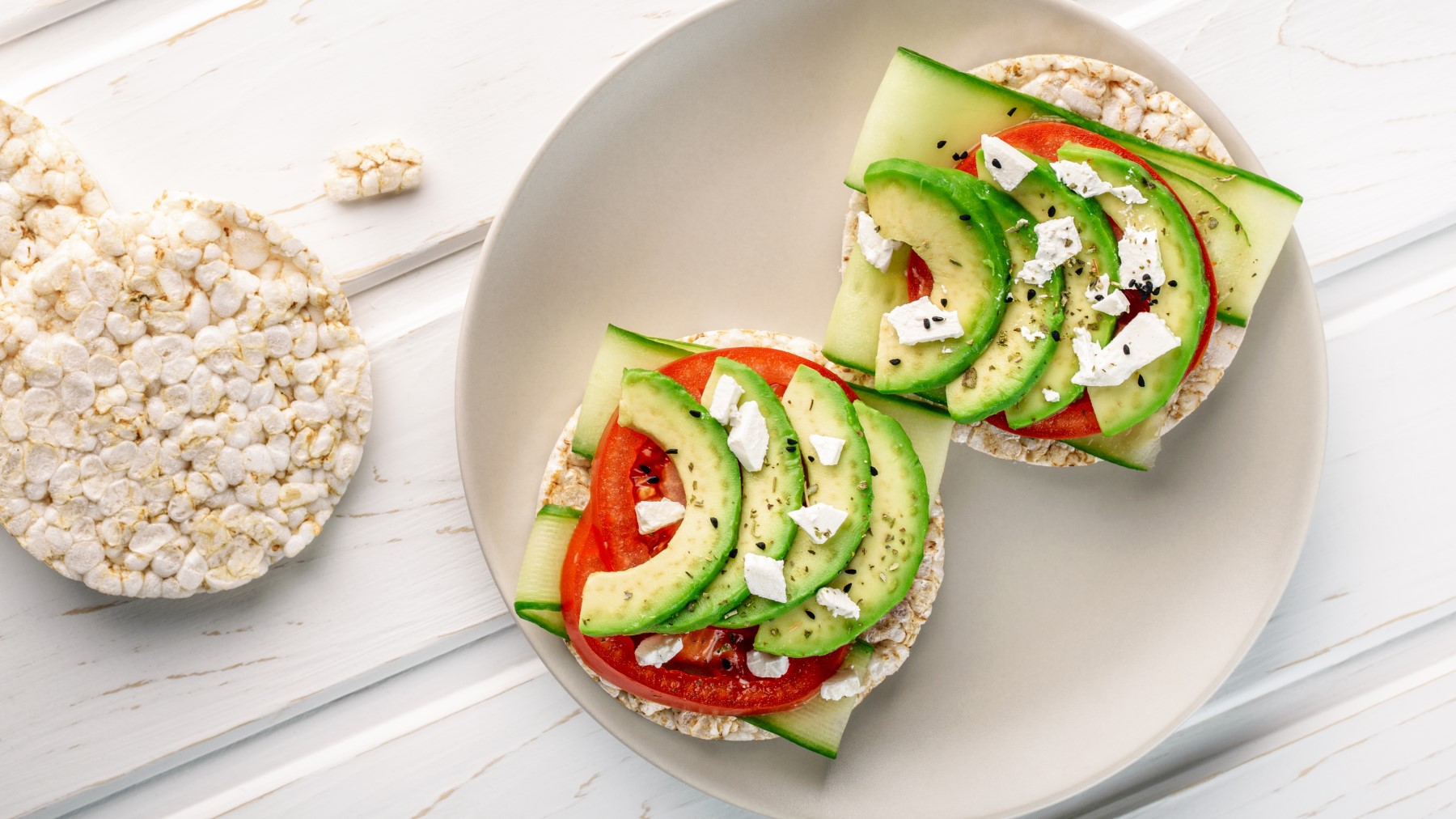 Reiswaffeln mit Avocado und Feta auf einem beigen Teller auf weißem Hintergrund.