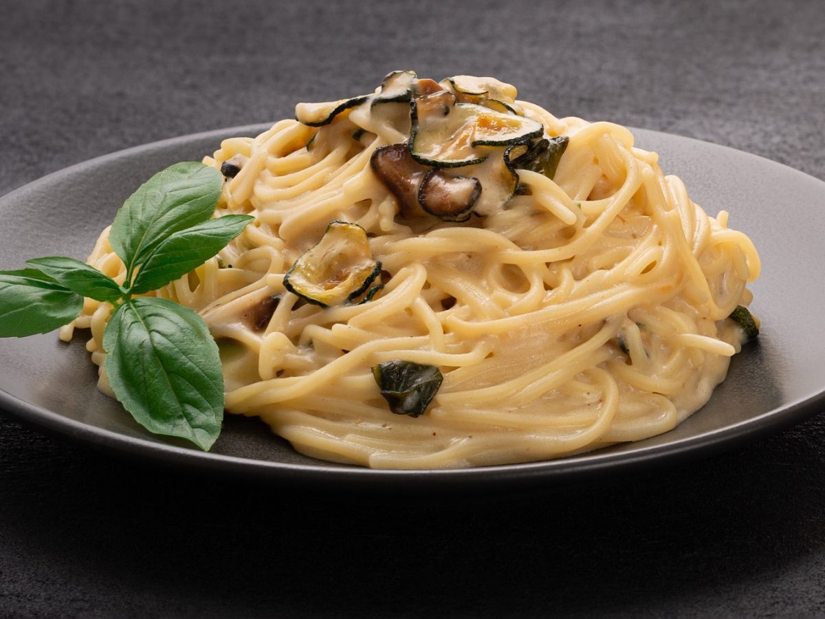 Spaghetti alla nerano auf einem schwarzen Teller von vorne fotografiert.