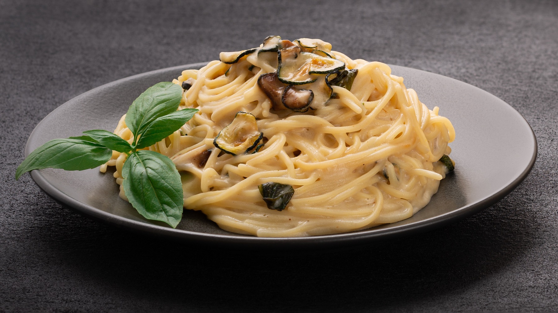 Spaghetti alla nerano auf einem schwarzen Teller von vorne fotografiert.