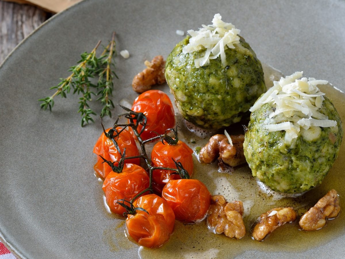 Vegane Spinatknödel mit veganer Butter und veganem Parmesan auf einem grauen Teller auf rot-weiß-kariertem Hintergrund.