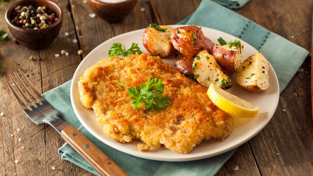 Veganes Cordon bleu serviert mit Kartoffeln auf einem weißen Teller auf hölzernem Hintergrund.