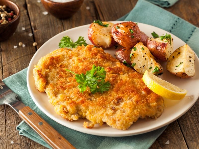 Veganes Cordon bleu serviert mit Kartoffeln auf einem weißen Teller auf hölzernem Hintergrund.