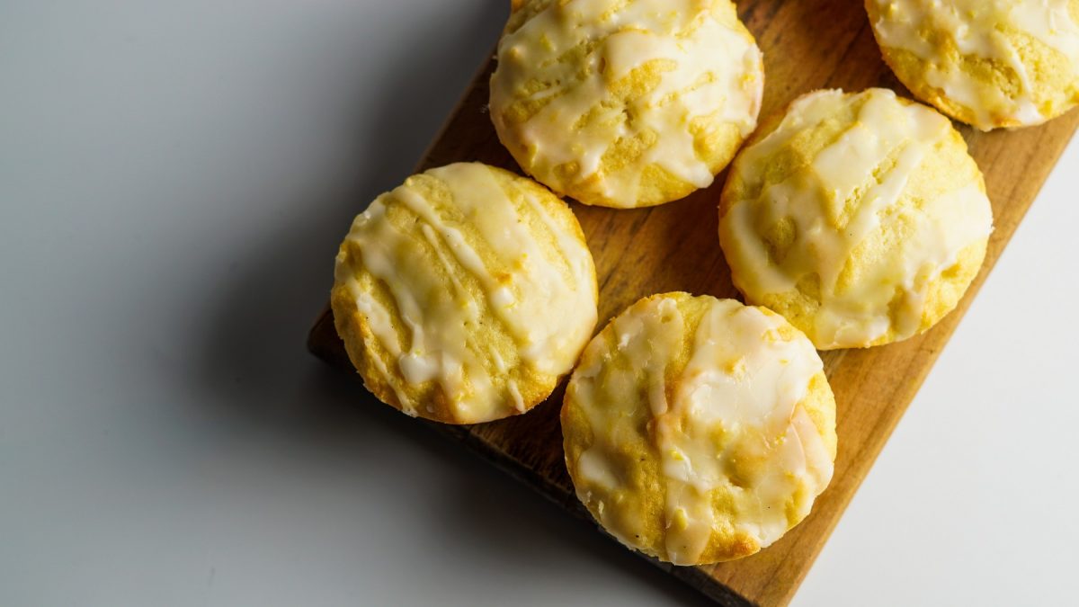 Zitronen-Muffins mit Zuckerguss auf einem Holzbrett von oben fotografiert vor einem weißen Untergrund.