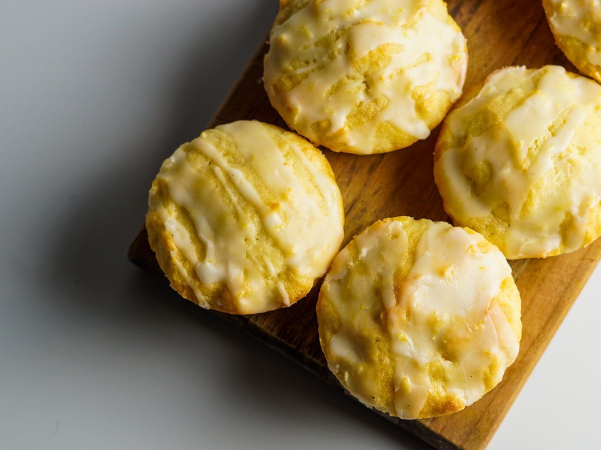 Zitronen-Muffins mit Zuckerguss auf einem Holzbrett von oben fotografiert vor einem weißen Untergrund.