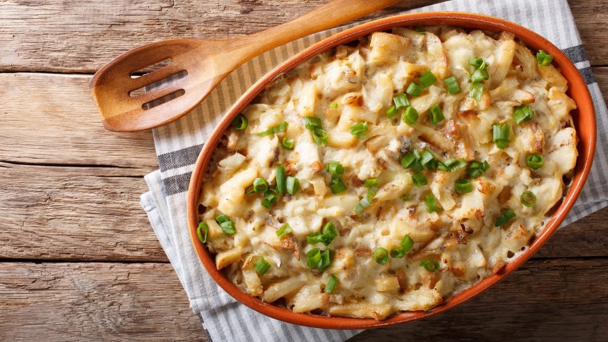 Bacalhau com natas in einer Keramikform von oben fotografiert, daneben ein Holzlöffel.