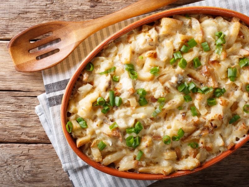 Bacalhau com natas in einer Keramikform von oben fotografiert, daneben ein Holzlöffel.