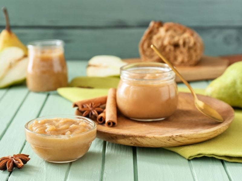 Birnenmarmelade in Schalen auf grünem Tisch, dekoriert mit Zimtstangen, Anissternen und frischen Birnen im Hintergrund.