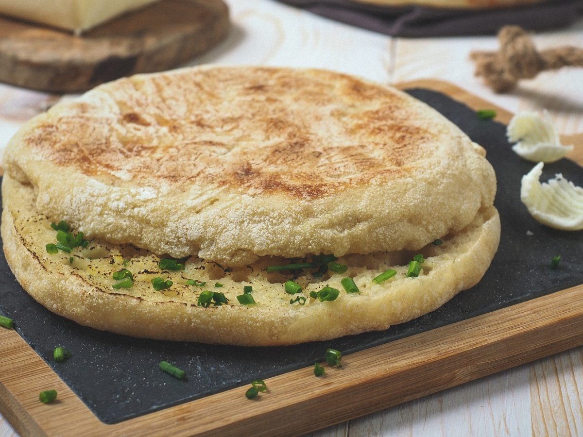 Aufgeschnittenes Bolo do caco mit Knoblauchbutter auf einer Steinplatte von vorne fotografiert.