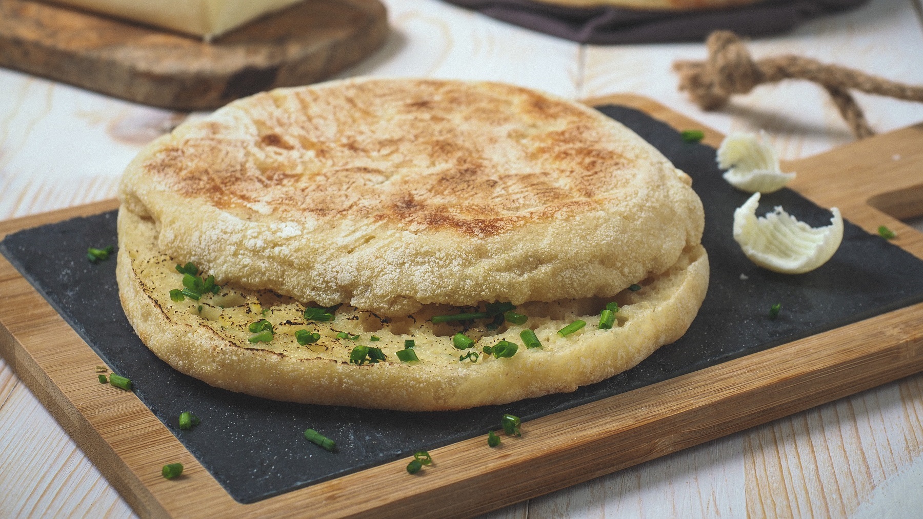 Aufgeschnittenes Bolo do caco mit Knoblauchbutter auf einer Steinplatte von vorne fotografiert.