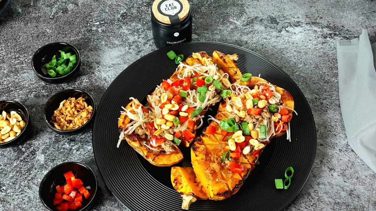 Gebackener Butternut-Kürbis Teriyaki mit Glasnudel-Salat auf einem schwarzen Teller auf grauem Hintergrund. Links davon kleine Schälchen.