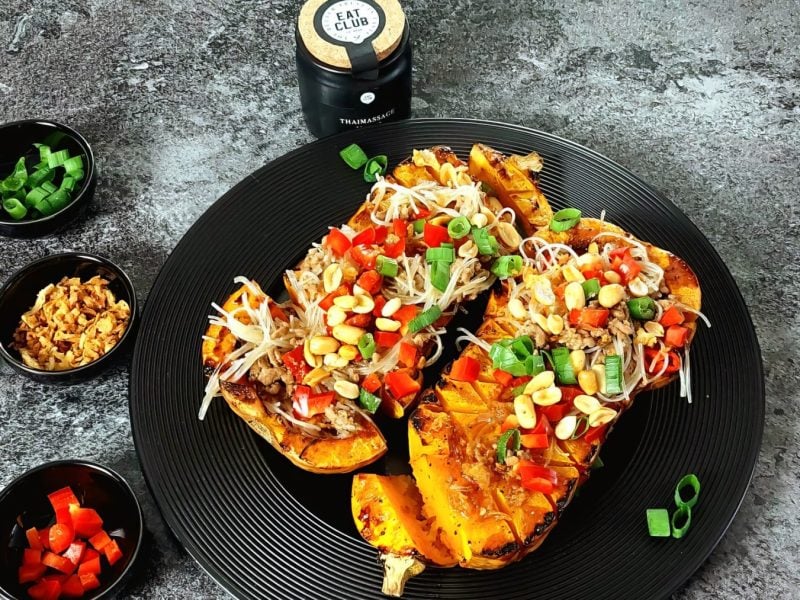 Gebackener Butternut-Kürbis Teriyaki mit Glasnudel-Salat auf einem schwarzen Teller auf grauem Hintergrund. Links davon kleine Schälchen.