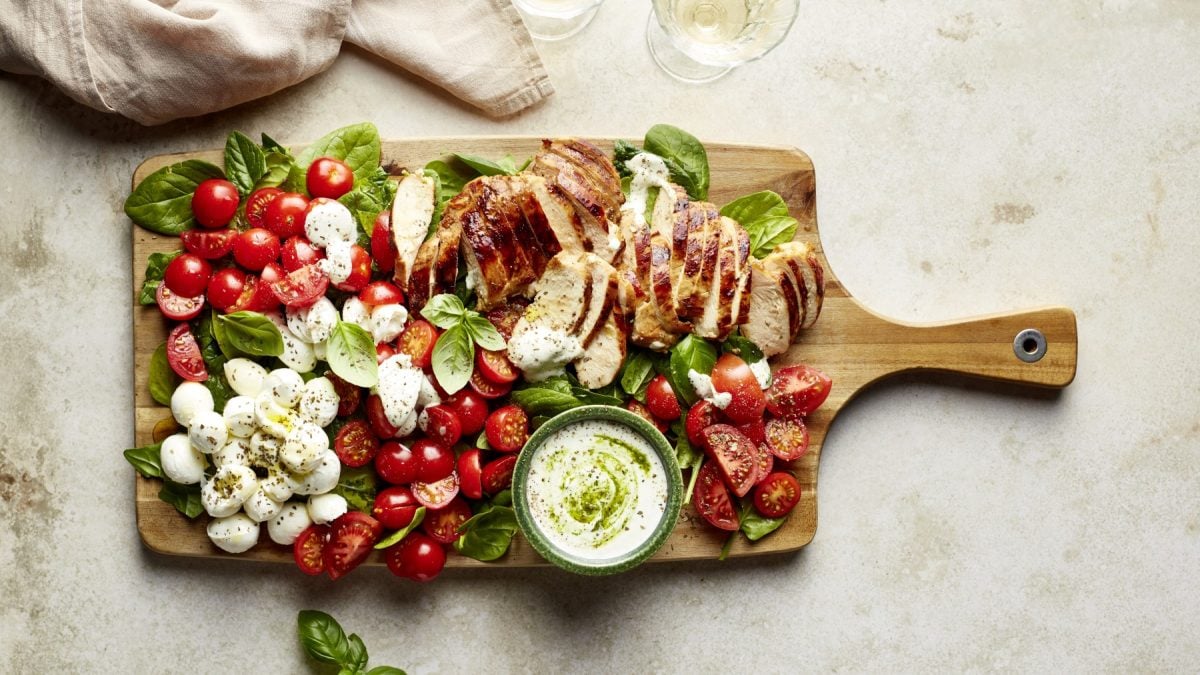 Draufsicht: Capreseboard "rapido" mit Balsamicohähnchen, Tomaten, Mozzarella und Basilikum auf Holzschneidebrett.