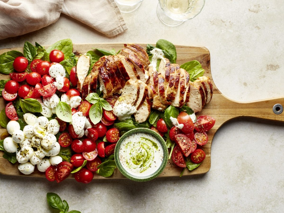 Draufsicht: Capreseboard "rapido" mit Balsamicohähnchen, Tomaten, Mozzarella und Basilikum auf Holzschneidebrett.