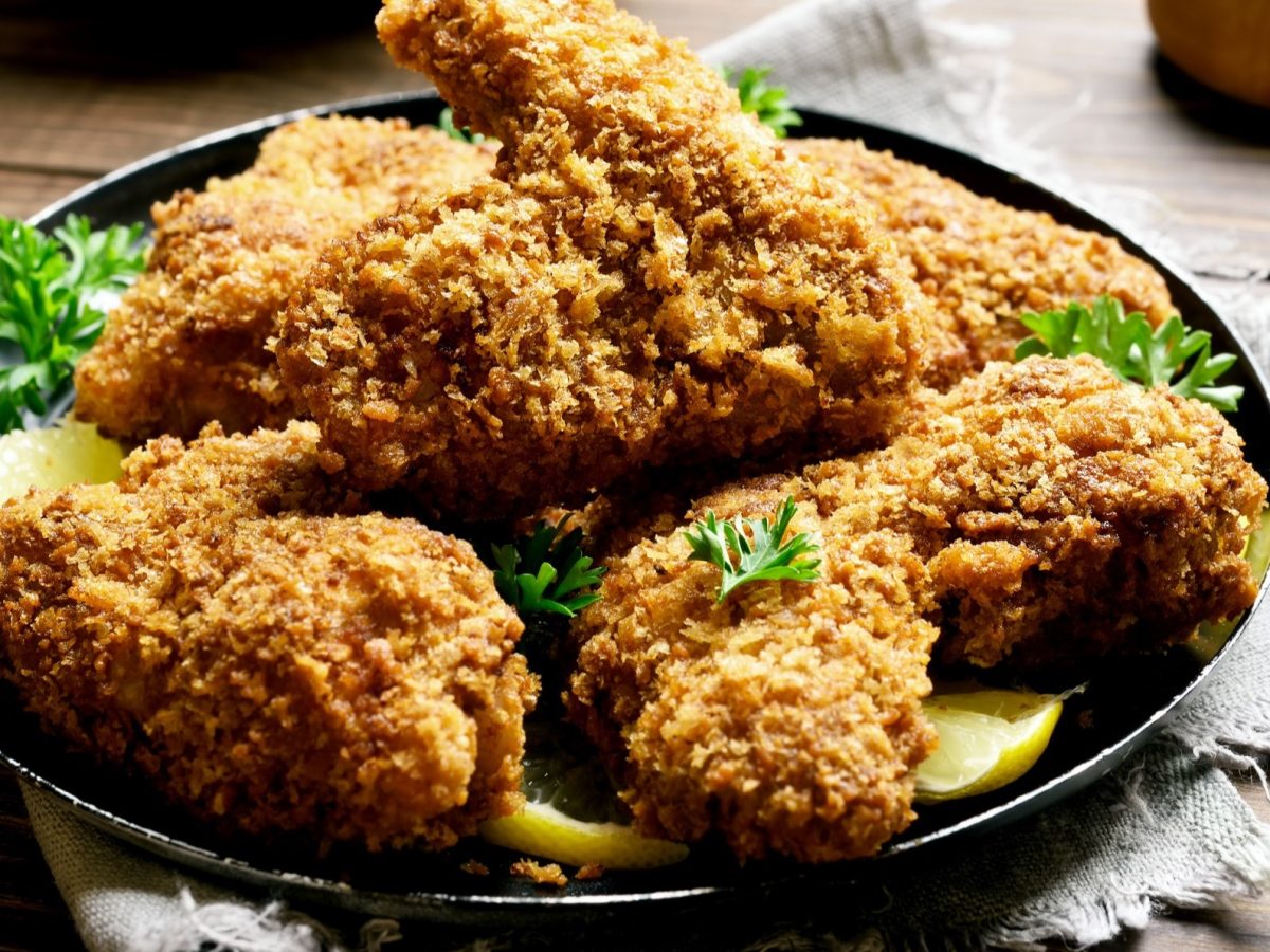 Draufsicht, leicht schräg: Mehrere ausgebratene Teile vom Backhendl auf einem dunklen Teller. Der steht auf einem robusten Holtisch.