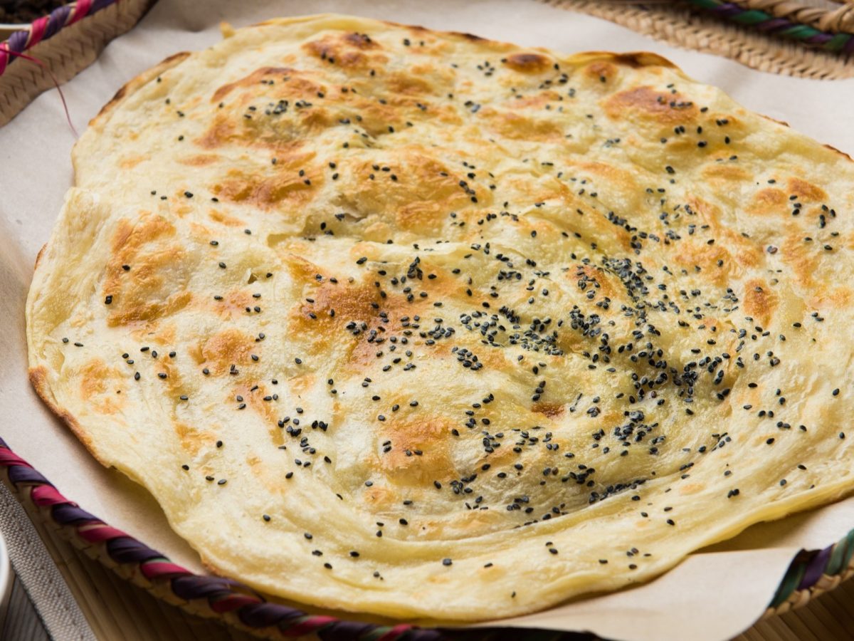 Draufsicht schräg: Ein rundes Pfannenbrot, dass mit Schwarzkümmel bestreut ist in einer gusseisernen Pfannen. Es wurde nach einen Malawach Pfannenbrot-Rezept zubereitet.