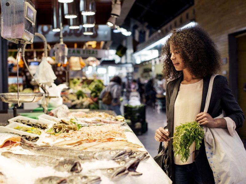 Frau auf einem Markt, die sich Fisch zum Kaufen in einer Auslage anschaut.