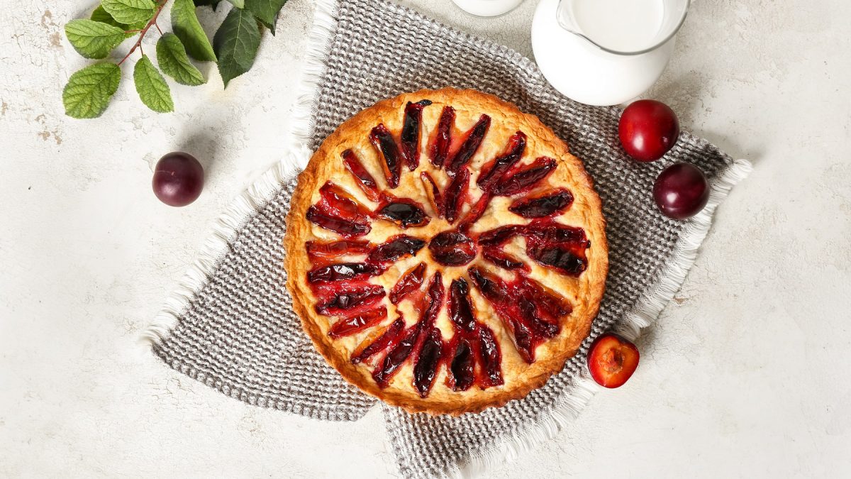 Frangipane-Tarte mit Pflaumen von oben fotografiert vor weißem Untergrund, daneben frische Pflaumen.