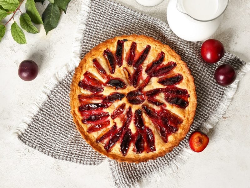 Frangipane-Tarte mit Pflaumen von oben fotografiert vor weißem Untergrund, daneben frische Pflaumen.