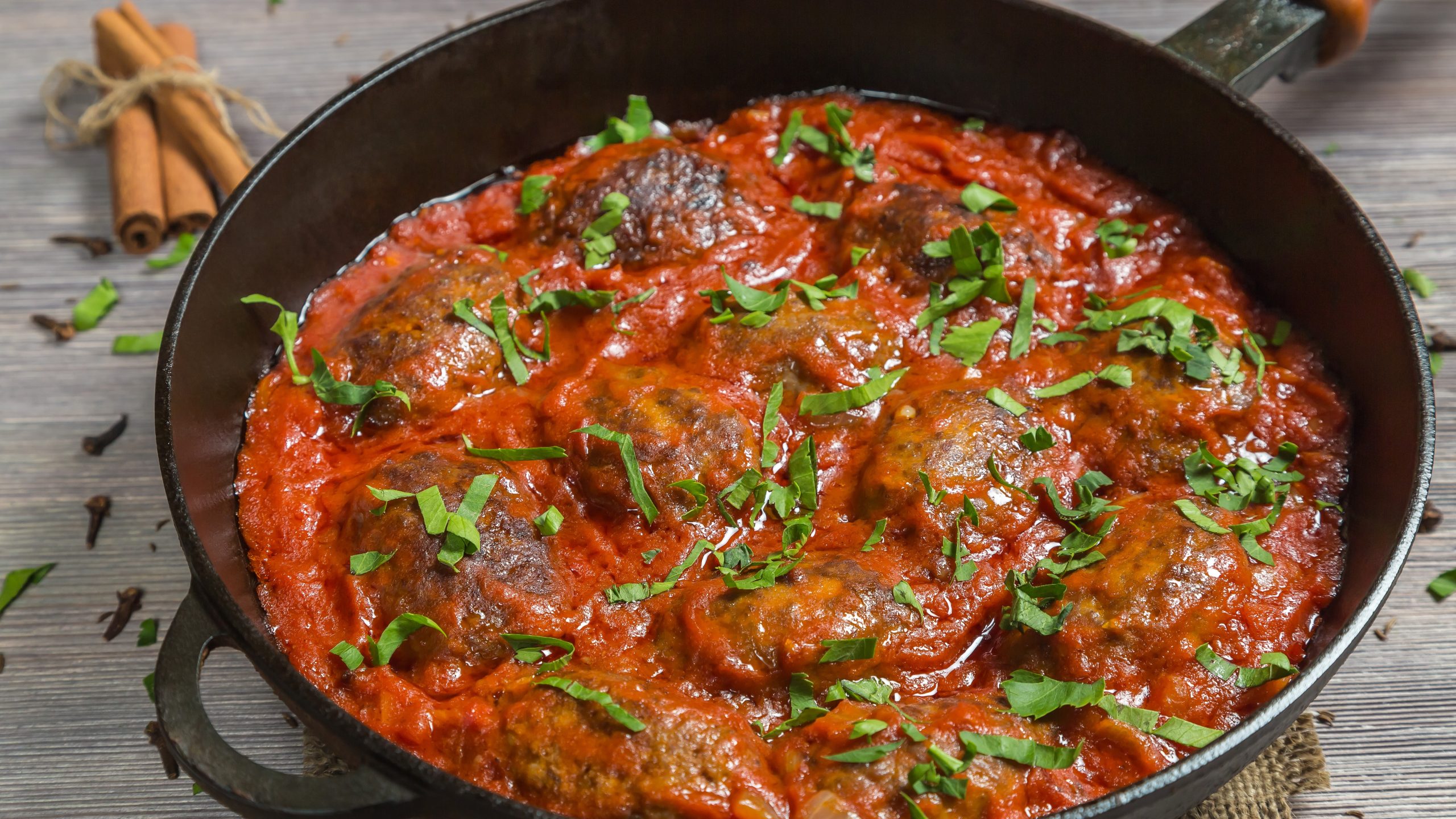 Eine gusseiserne Pfanne mit den Hackbällchen in Tomatensauce von oben auf einem rustikalen Holztisch fotografiert.